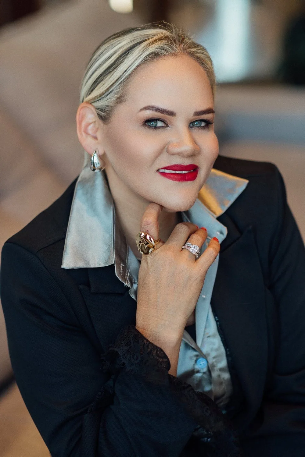 Paula Teixeira sorrindo, de blazer preto e camisa prateada